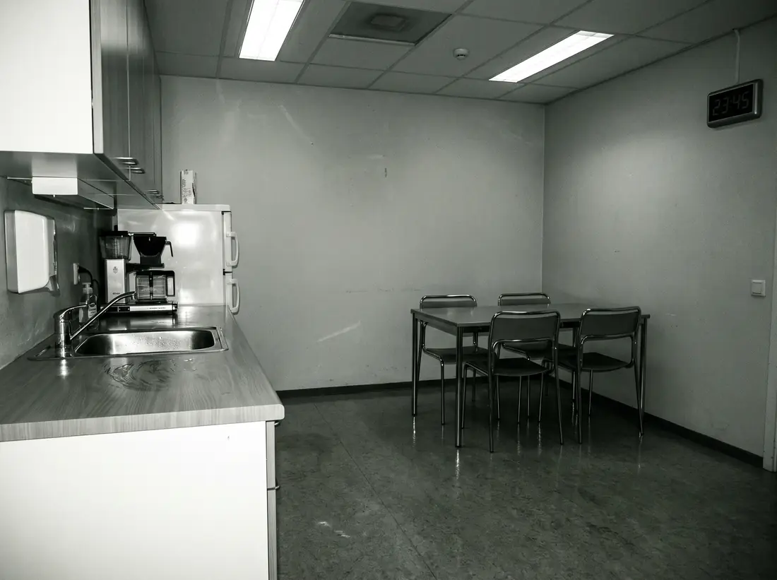 An empty office break room at night, worktops wiped and chairs pushed in.